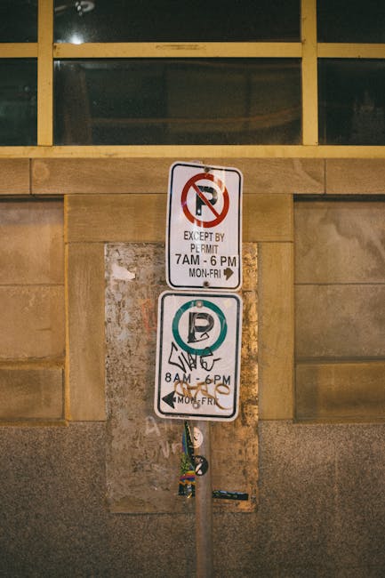 Four blue parking permit signs mounted on black metal poles, positioned against a modern metallic building facade with vertical ridges. The signs display a white 'P' indicating parking privileges, wit